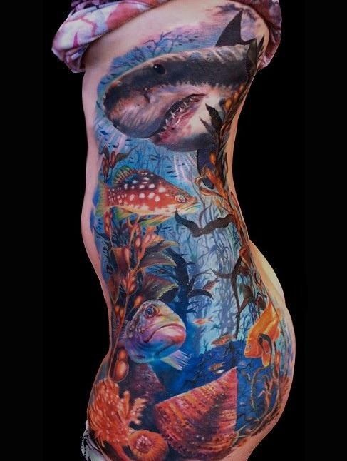 Tatuaje en las costillas de un gran tiburón coloreado y los habitantes del mar.