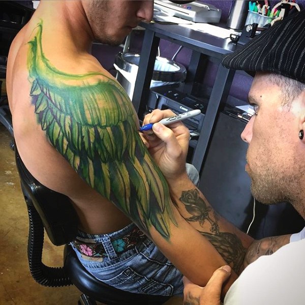 Big green colored pan colored wings tattoo on arm and shoulder