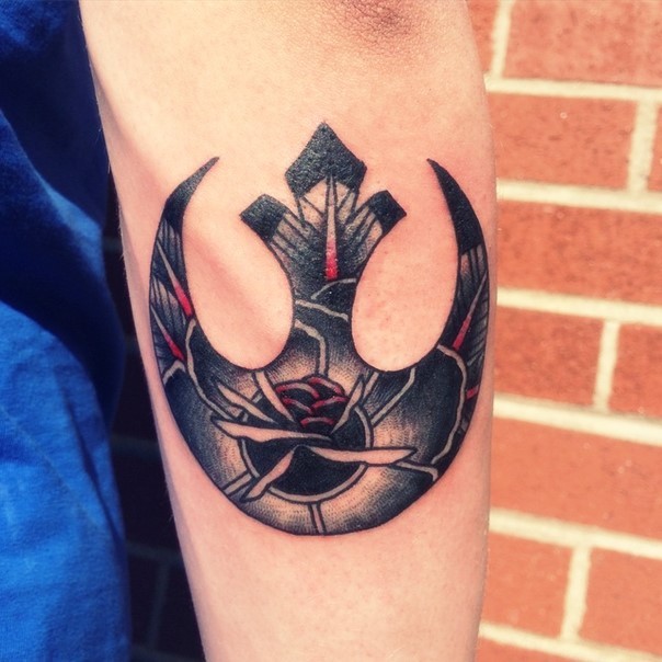 Big usual shaped Rebel Alliance emblem tattoo on forearm stylized with flower