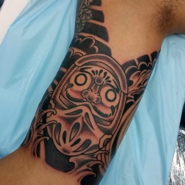 Black and gray style colored biceps tattoo of daruma doll