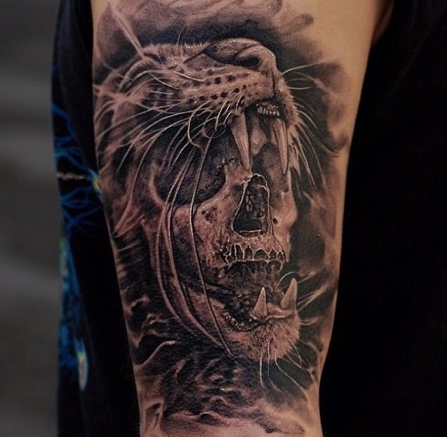 Black and gray style colored shoulder tattoo of creepy skull with cat skin helmet