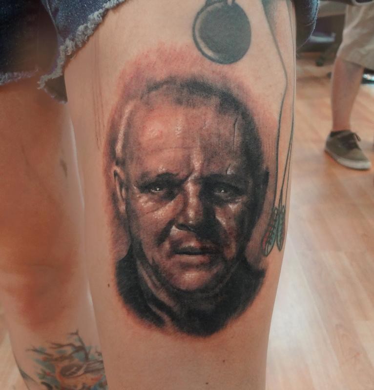 Black and gray style colored thigh tattoo of Hannibal Lector portrait