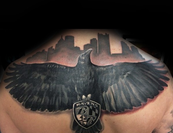 Black and gray style colored upper back tattoo of big crow with emblem and lettering
