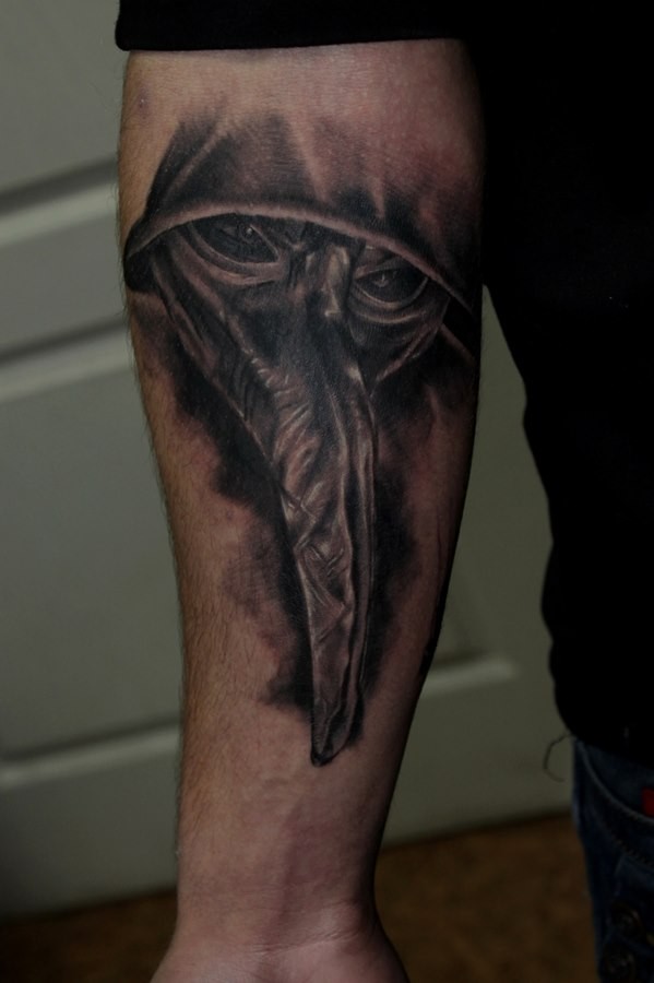 Black and gray style creepy looking plague doctor tattoo on forearm