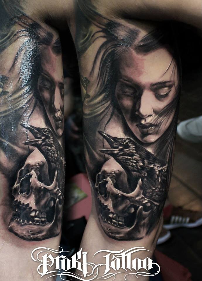 Black and gray style detailed biceps tattoo of woman face with skull and crow