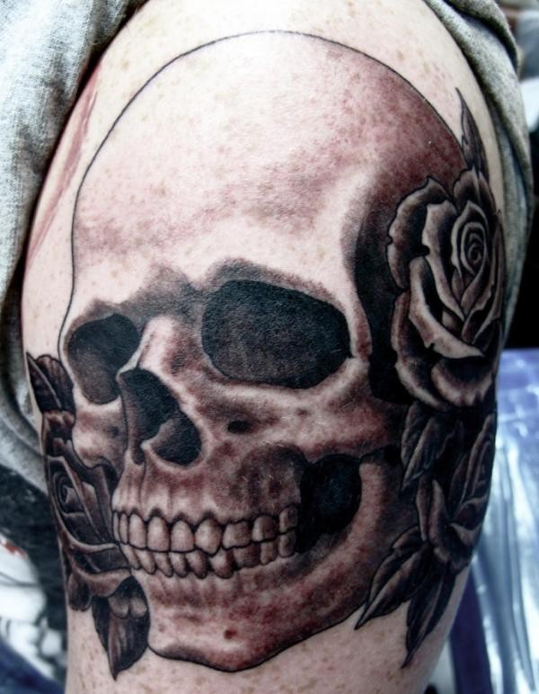 Black and gray style shoulder tattoo of human skull and flowers