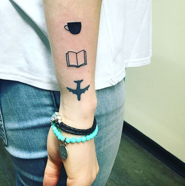 Tatuaje en el antebrazo, taza, libro abierto y avión