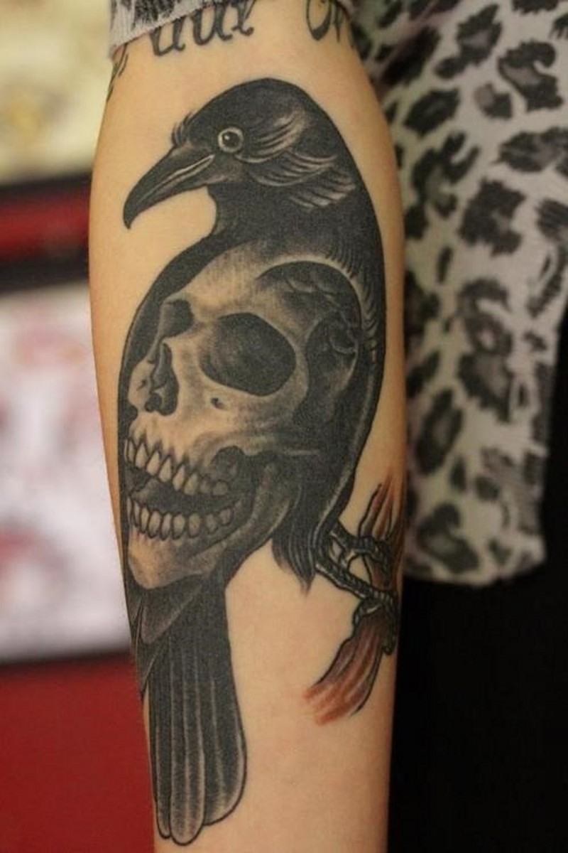 Black crow on branch stylized with big human skull detailed old style forearm tattoo
