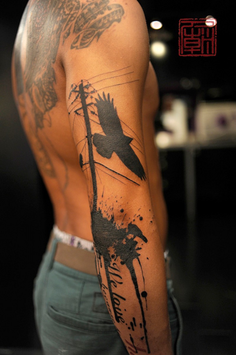 Black flying crow and power line tattoo on arm with lettering and paint drips