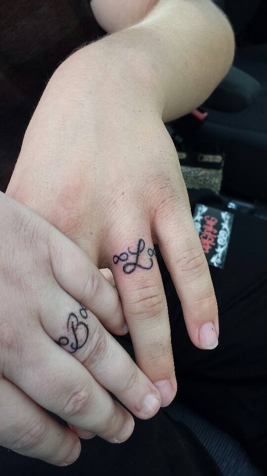 Black ink cute ring shaped infinity symbols couple tattoo on ring fingers with letters in center