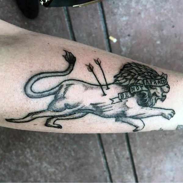 Black ink engraving style forearm tattoo of lion with arrows and lettering