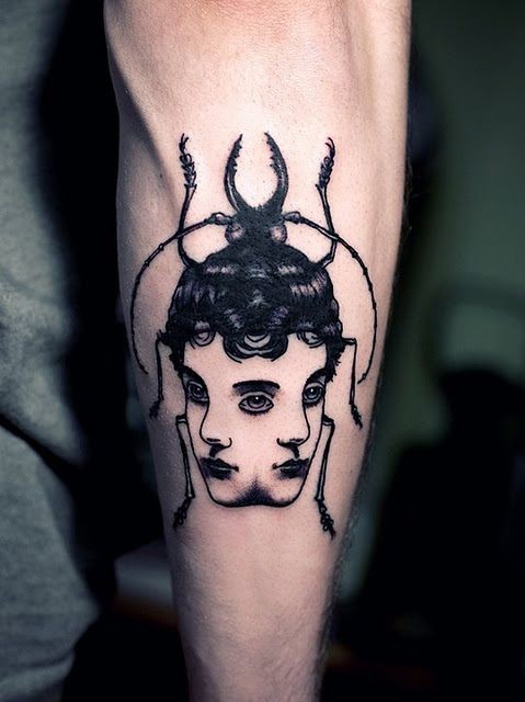 Tatuaje en el antebrazo,
escarabajo negro surrealista con dos caras de chicas