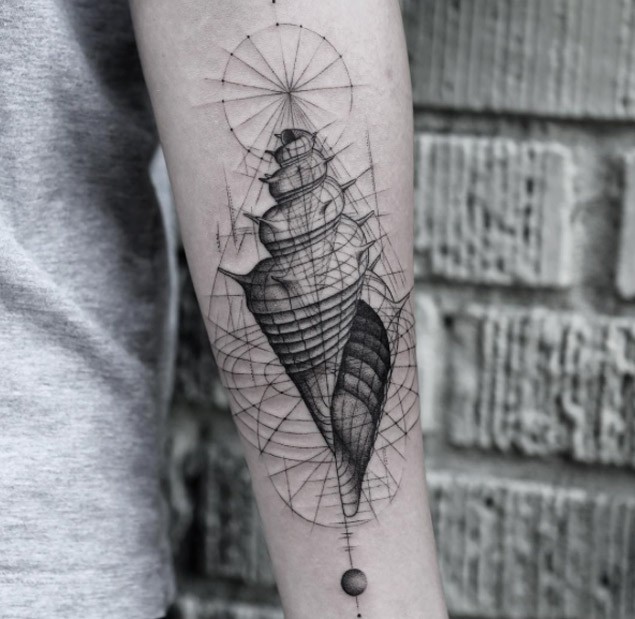 Black ink forearm tattoo of small shell with ornaments