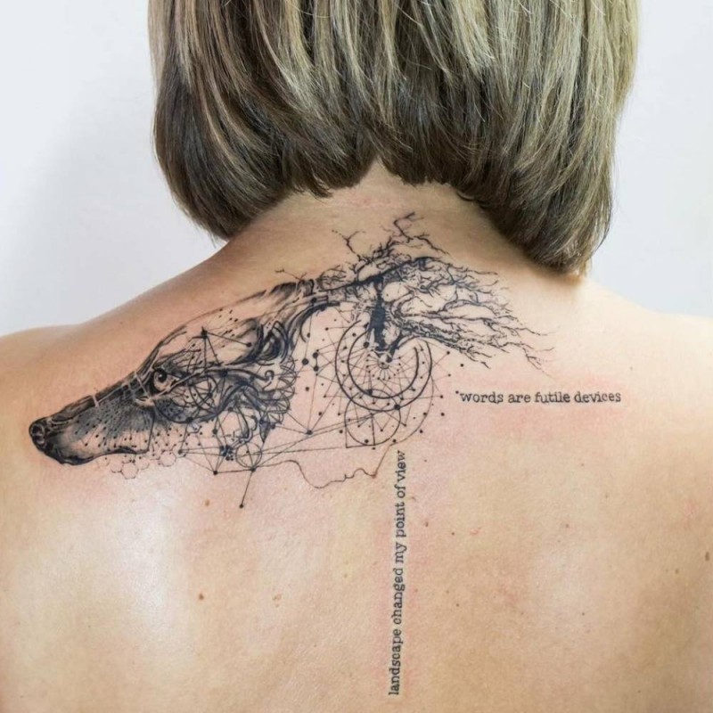 Black ink upper back tattoo of wolf with lettering and ornaments