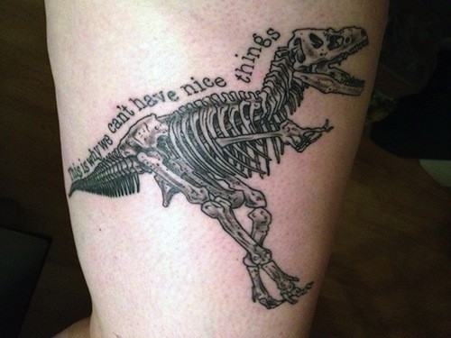 Black ink very detailed biceps tattoo of dinosaur skeleton with lettering