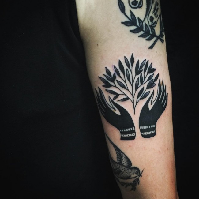 Blackwork style arm tattoo of human hands and tree branch