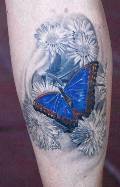Tatuaggio colorato sulla gamba la farfalla blu tra i fiori