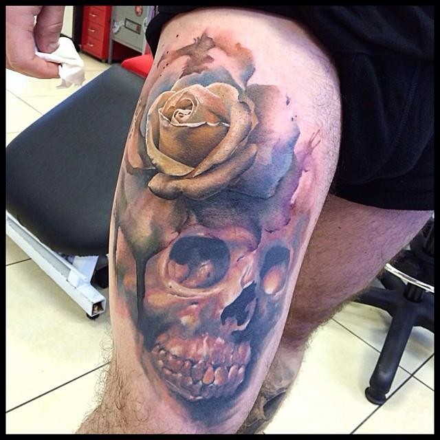 Atemberaubendes sehr detailliertes farbiges Oberschenkel Tattoo mit der Rose Blume und menschlichem Schädel