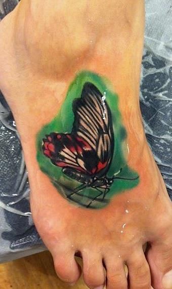 Tatuaggio colorato 3D sui piedi la farfalla sul fondo verde