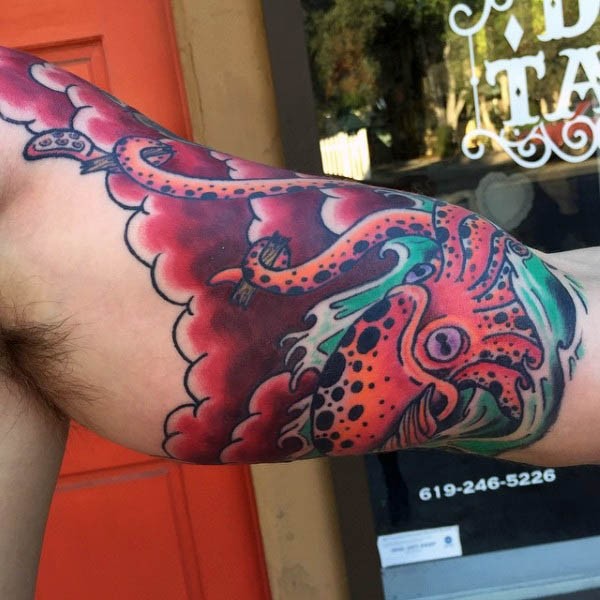 Cartoon like painted and colored big  squid in sea tattoo on biceps