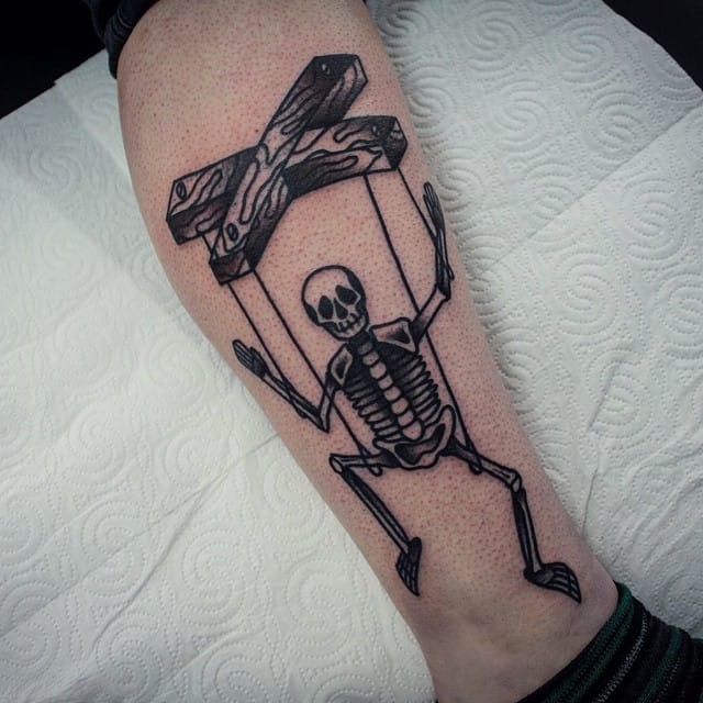 Cartoon style black ink leg tattoo of small dancing skeleton puppet