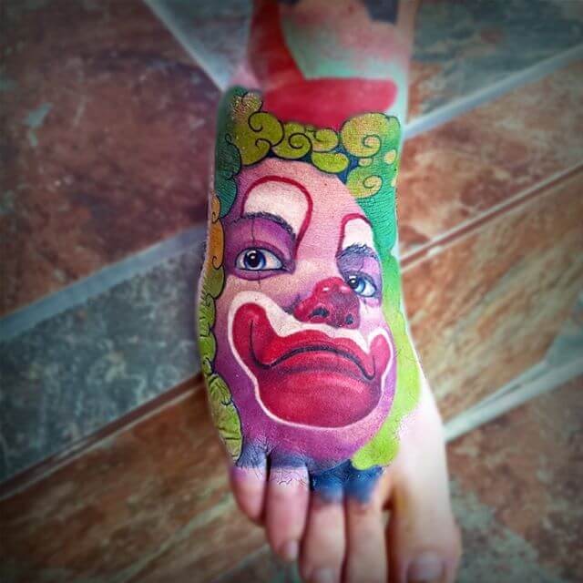 Cartoon style colored foot tattoo of creepy clown face
