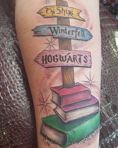Cartoon style colored forearm tattoo of fantasy road sign with books