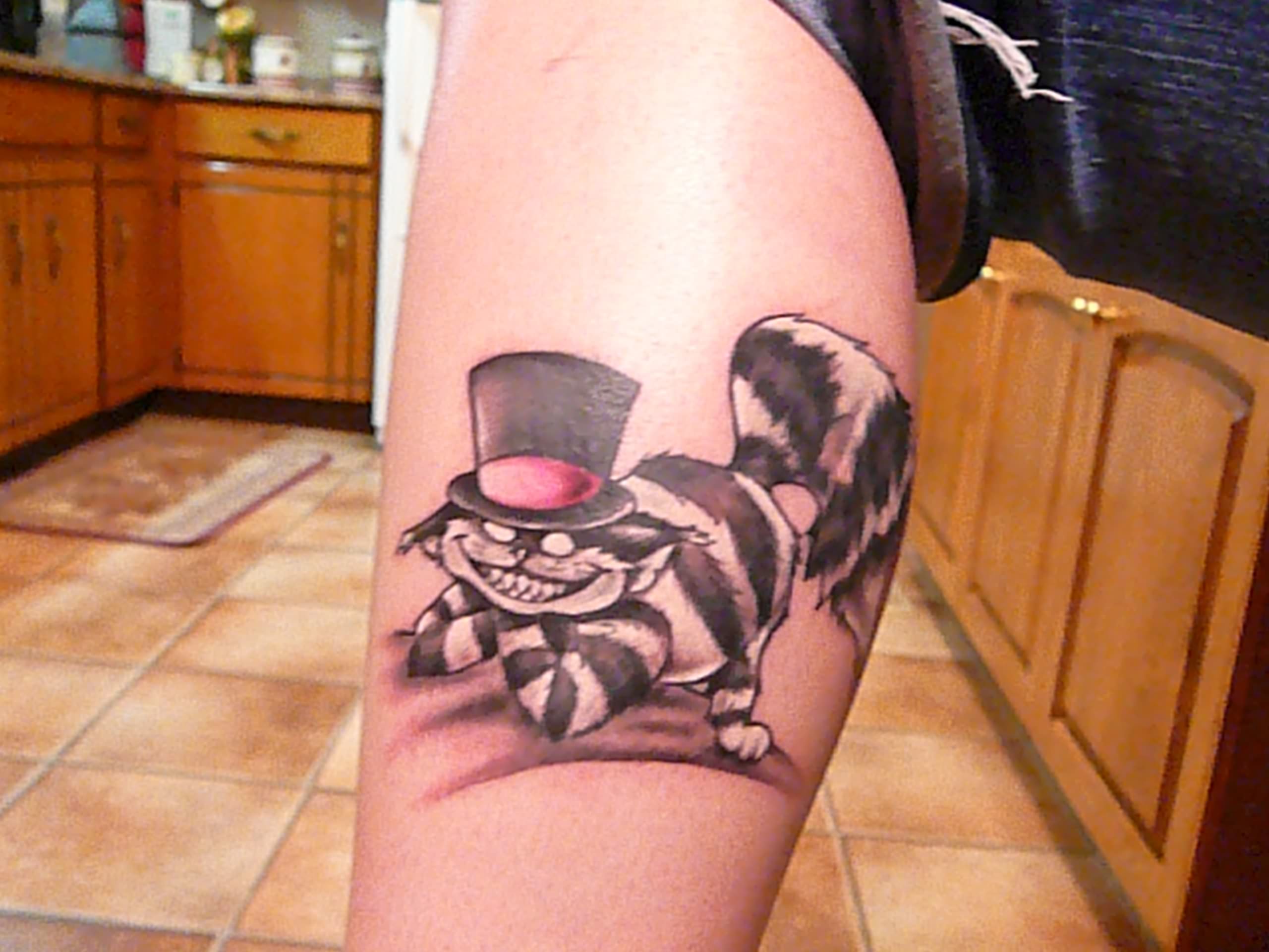 Tatuaggio carino sulla gamba il gatto Cheshire con il capello