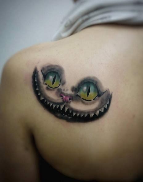 Cheshire cat&quots smile and look colored fairy tale tattoo on lady&quots shoulder blade