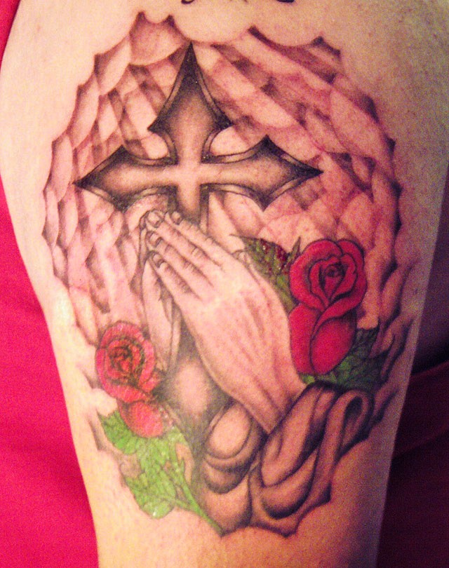 Tatuaje en el brazo, cruz de hierro con manos que oran y rosas, estilo cristiano