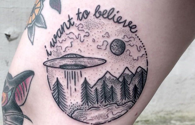 Circle shaped black ink mountain forest and alien ship tattoo combined with lettering