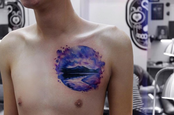 Circle shaped watercolor chest tattoo of big lake near high mountains