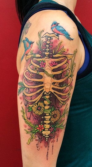 Coloreada guapa pintada por Dino Nemec tatuaje en el brazo superior del esqueleto humano con flores y pájaros