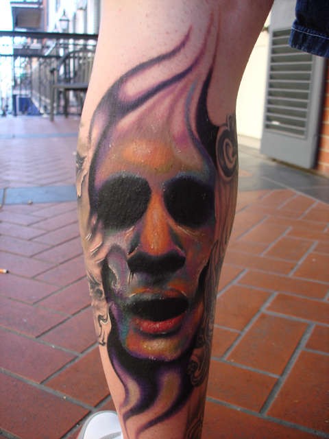 Colored horror style terrifying face tattoo on leg muscle