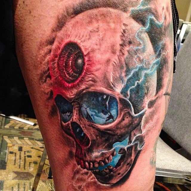 Colored medium size thigh tattoo of fantasy skull with eye and lightning