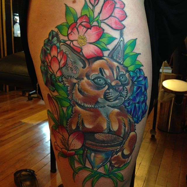 Colorful illustrative style thigh tattoo of small caracal with flowers
