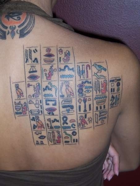 Tatuaje en la espalda coloreado de jeroglíficos egipcios.