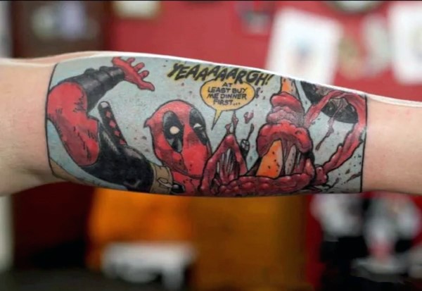 Comic books style colored arm tattoo of funny Deadpool with lettering
