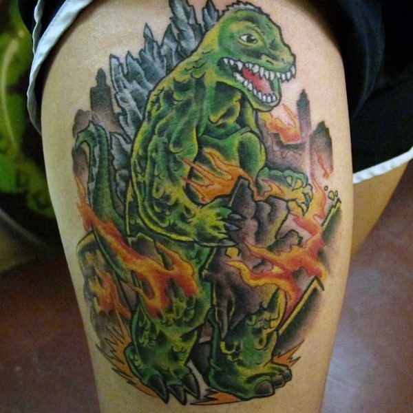 Cool cartoon like multicolored Godzilla with burning city tattoo on thigh