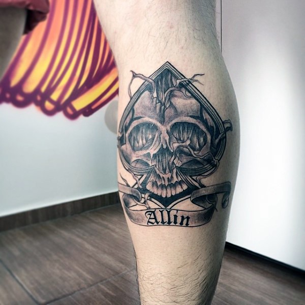 Cool designed black ink spades symbol stylized with skull and lettering tattoo on leg