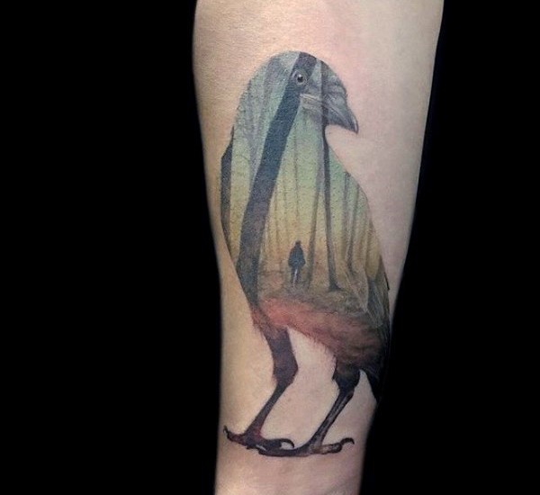 Cool looking colored forearm tattoo of crow with human in forest