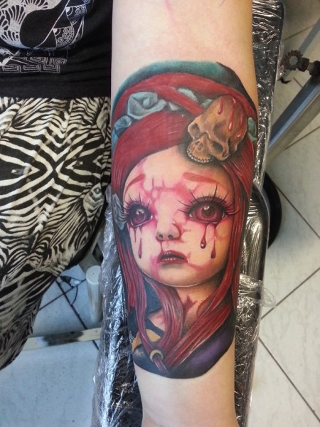 Creepy horror like colored crying with bloody tears doll tattoo on forearm