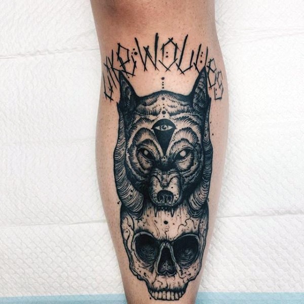 Creepy looking black ink leg tattoo of creepy skull with wolf head and lettering