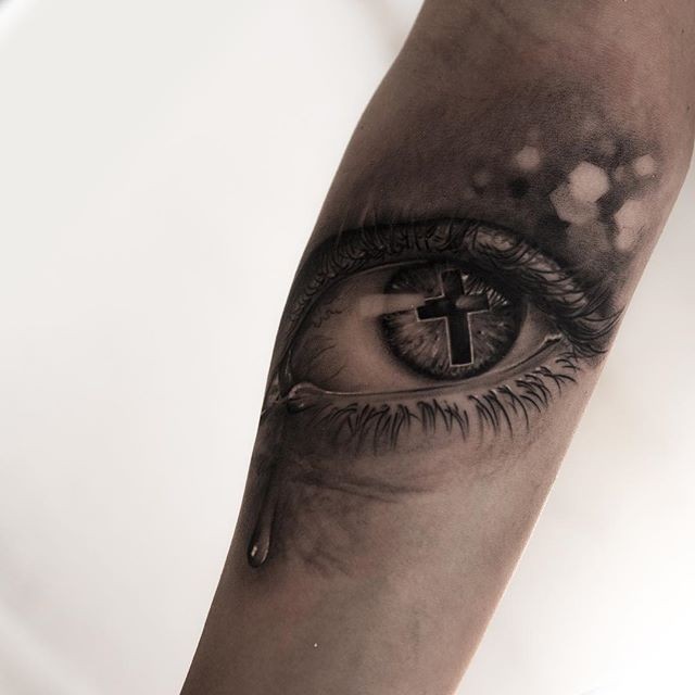 Tatuaje en el antebrazo, ojo gris con cruz en pupila