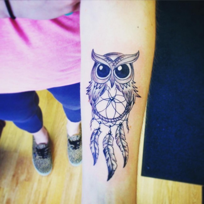 Cute cartoon style black ink forearm tattoo of owl with dream catcher