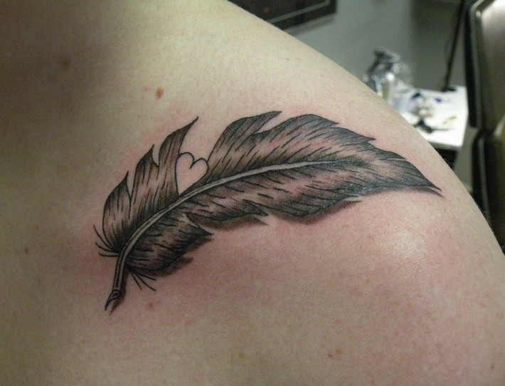 Cute gray-ink feather with white heart tattoo on shoulder