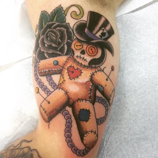 Nettes mehrfarbiges Bizeps Tattoo mit Gentleman Voodoo-Puppe und schwarzer Rose mit Schmuck