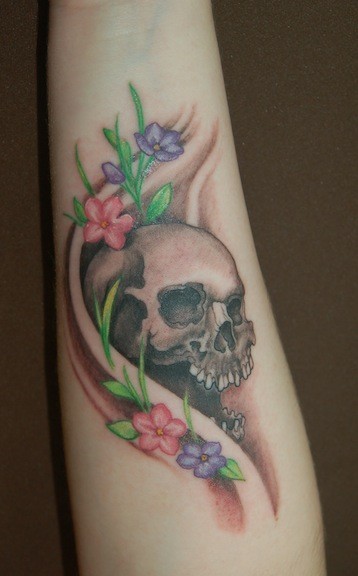Tatuaje en el antebrazo, cráneo con flores el la piel