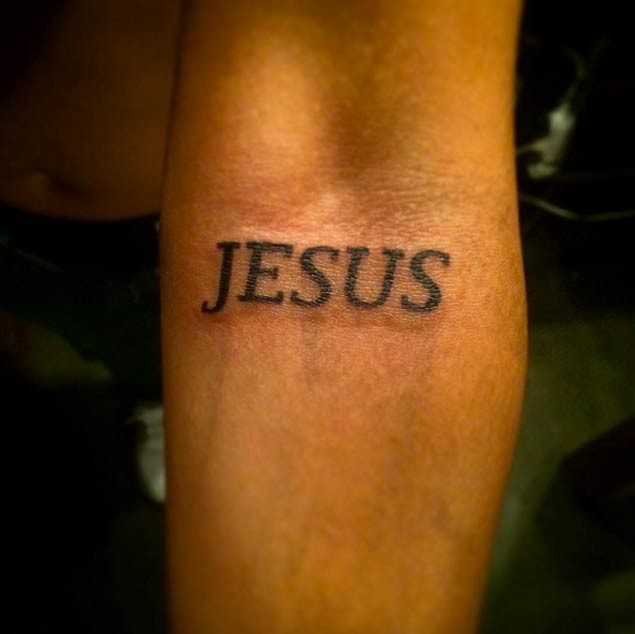 Dunkle schwarze Beschriftung &quotJesus" religiöses Tattoo am Unterarm