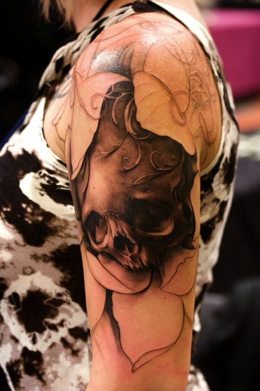 Tatuaje  de cráneo negro con hojas blancas en el brazo